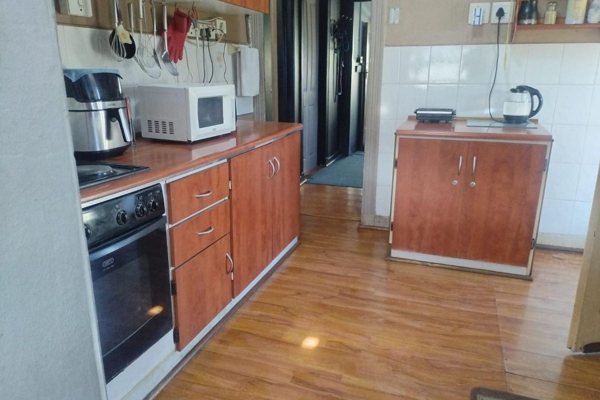 A functional kitchen featuring wood-look laminate cabinetry, built-in oven, hob, and tiled splashbacks, offering a practical layout with potential for modern updates.