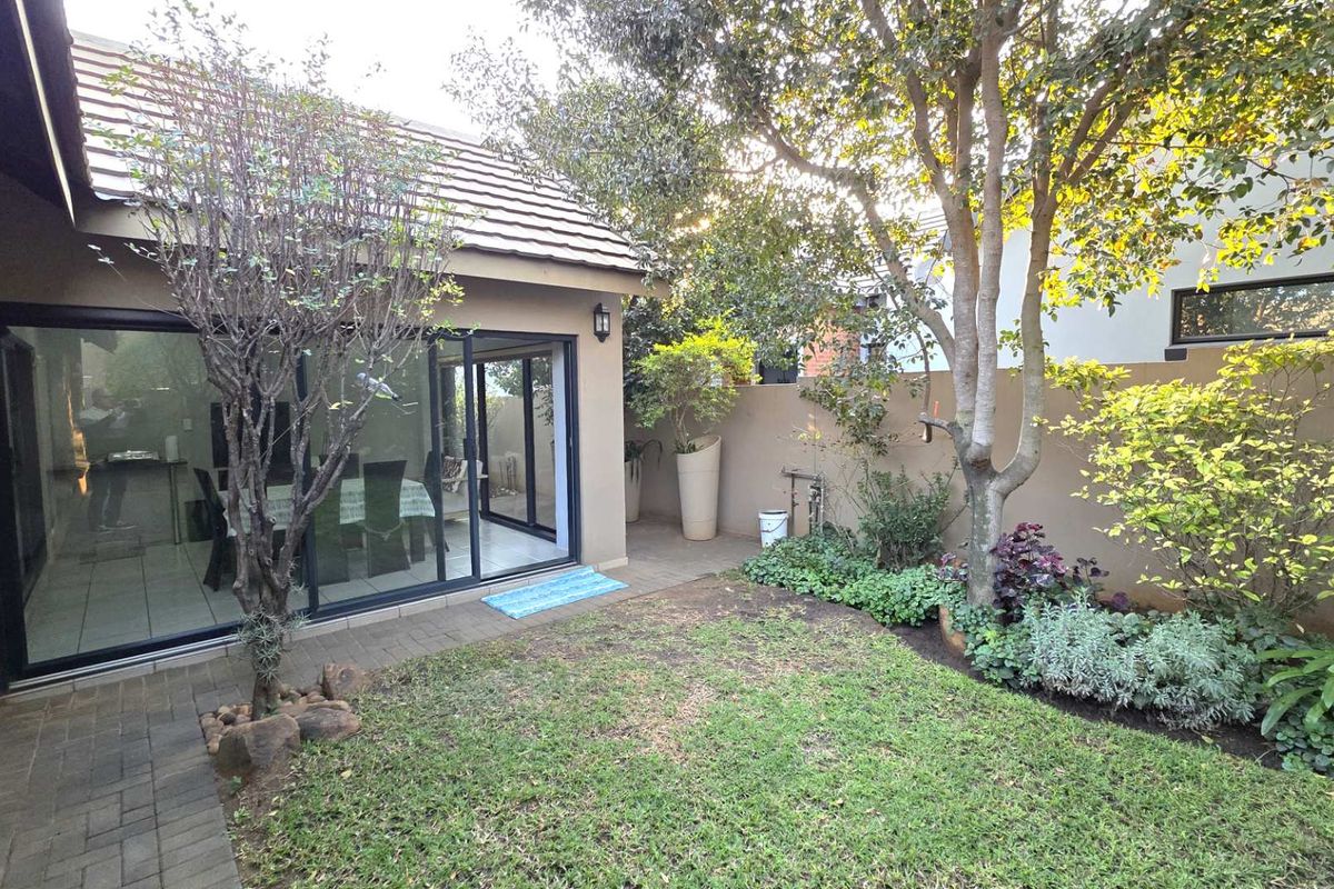 A private rear garden featuring a paved patio area, established trees, and sliding glass doors providing seamless access to the interior living space.