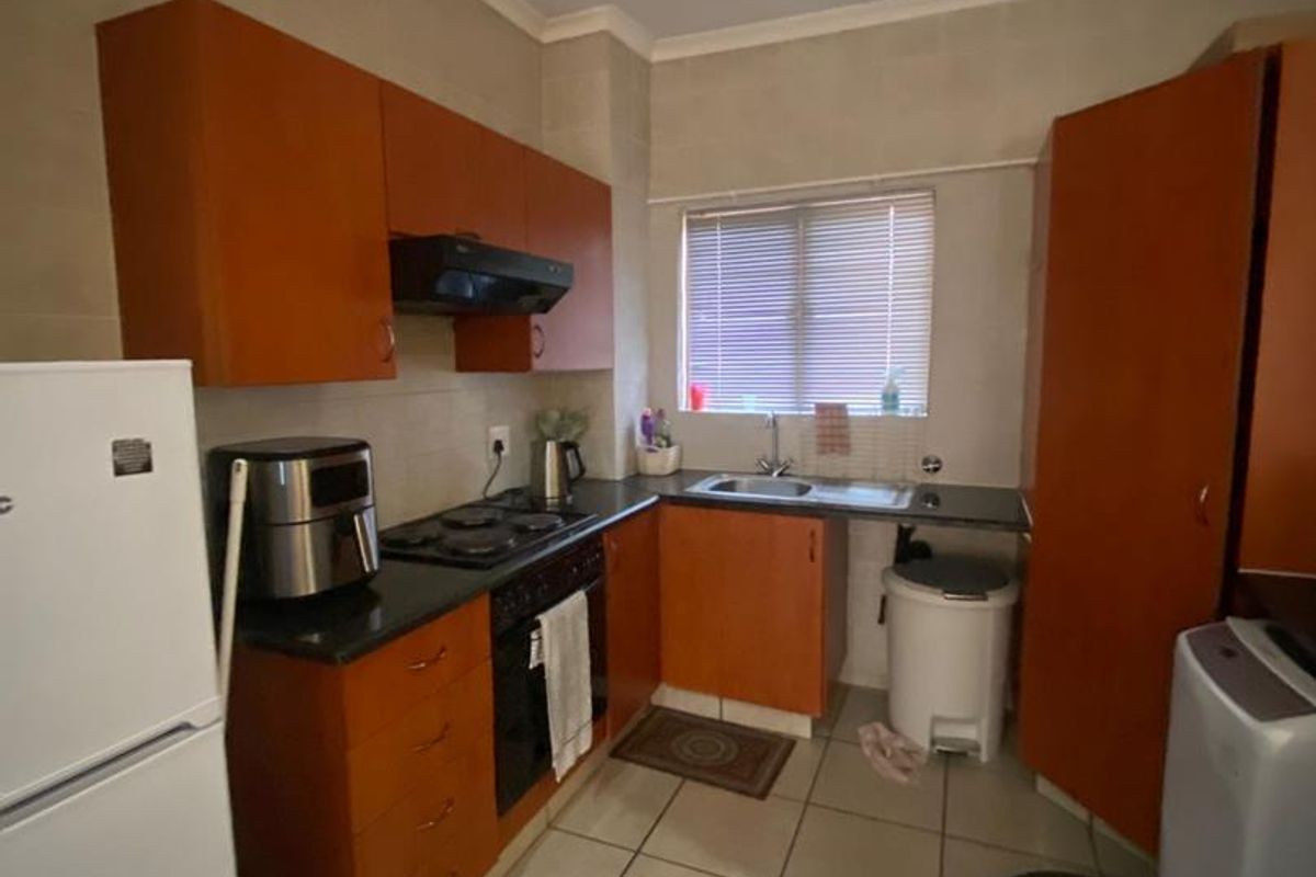 A functional kitchen featuring wooden cabinetry, dark countertops, a built-in oven, hob, extractor fan, and a stainless steel sink.