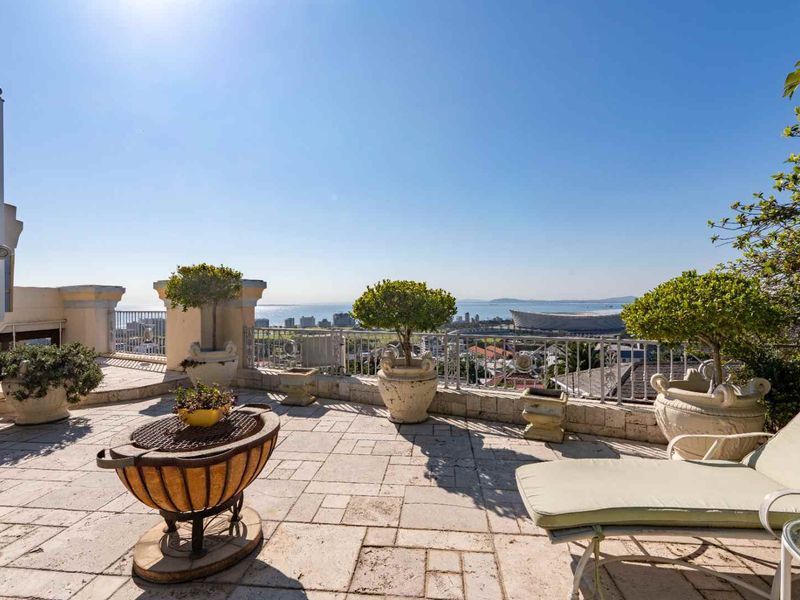 Spacious outdoor balcony featuring stone tile flooring, a protective metal balustrade, and panoramic coastal and city views.