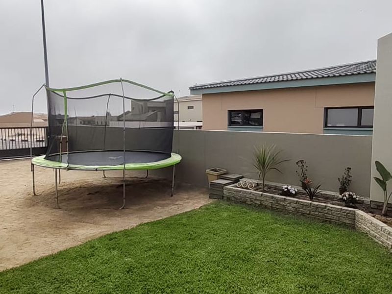 A rear garden area featuring a small lawn, a raised stone-clad planter bed, a paved section, and a built-in braai facility.