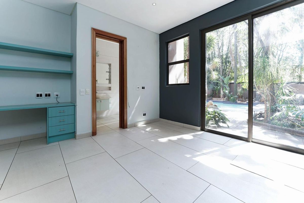 A bright bedroom featuring large sliding glass doors with pool views, built-in desk cabinetry, and an en-suite bathroom entrance.