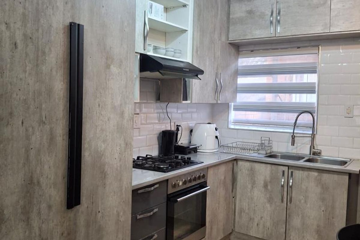 Modern kitchen featuring wood-look cabinetry, subway tile backsplash, gas hob, built-in oven, and double sink with tiled flooring.