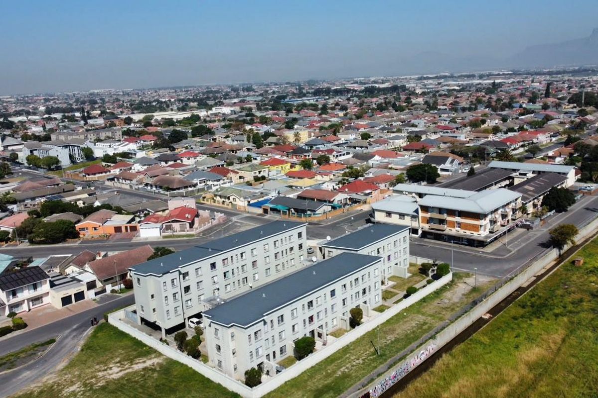 Aerial view of a multi-story apartment complex situated within a residential neighborhood, featuring paved access and perimeter boundary walls.