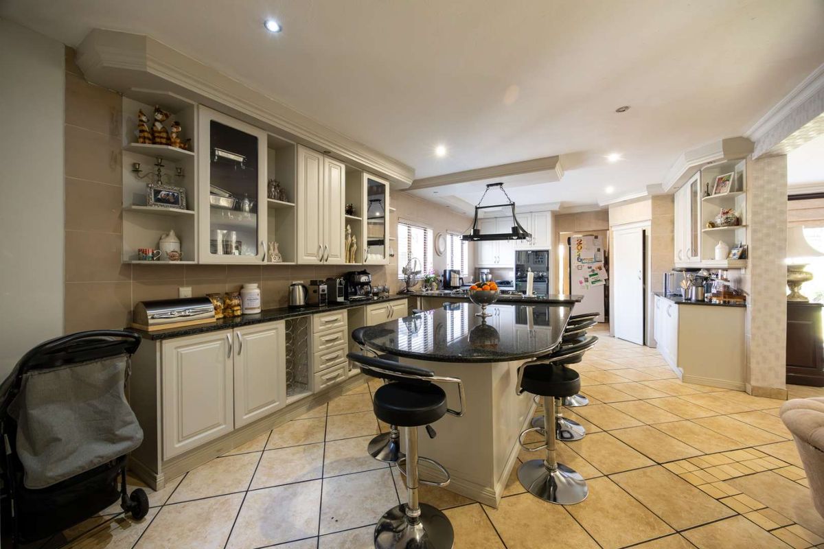 Spacious kitchen featuring a large central island with granite countertops, ample built-in cabinetry, and tiled flooring, offering a functional and well-lit cooking space.