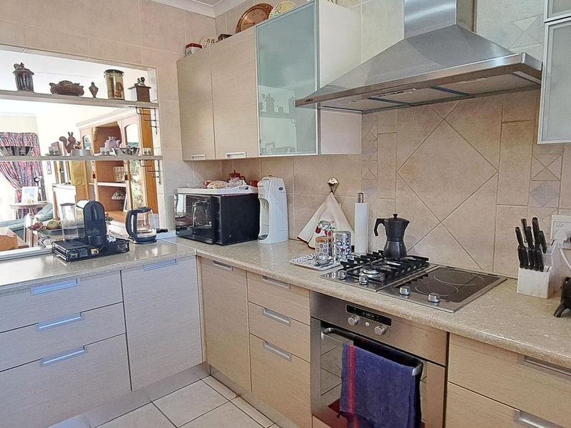 Functional kitchen featuring light wood cabinetry, stone-look countertops, a dual gas and electric hob, stainless steel extractor fan, and a convenient pass-through window.