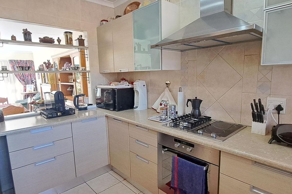 Functional kitchen featuring light wood cabinetry, stone-look countertops, a dual gas and electric hob, stainless steel extractor fan, and a convenient pass-through window.