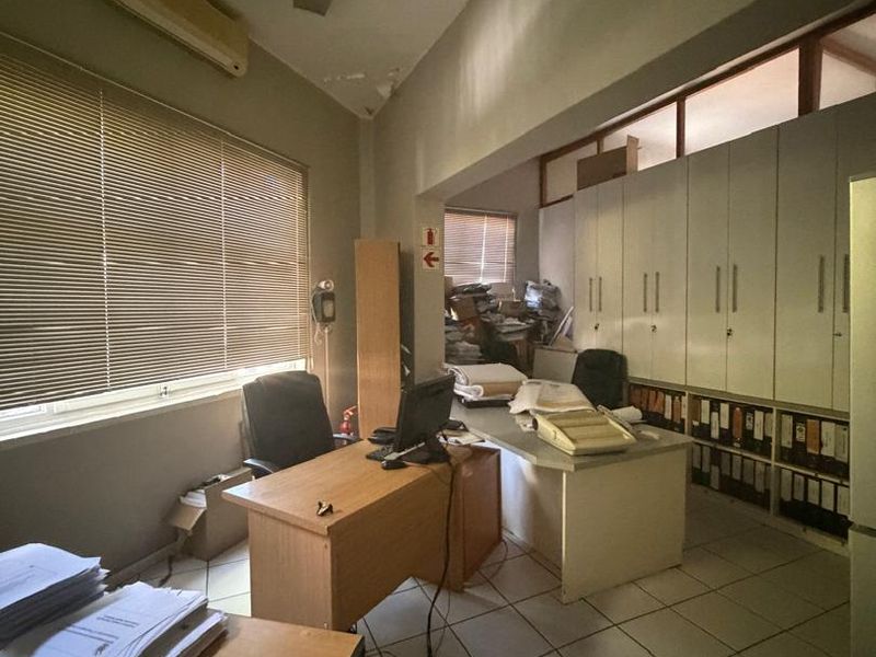 A functional office space featuring built-in storage cabinetry, tiled flooring, and a wall-mounted air conditioning unit, currently used as a workspace.