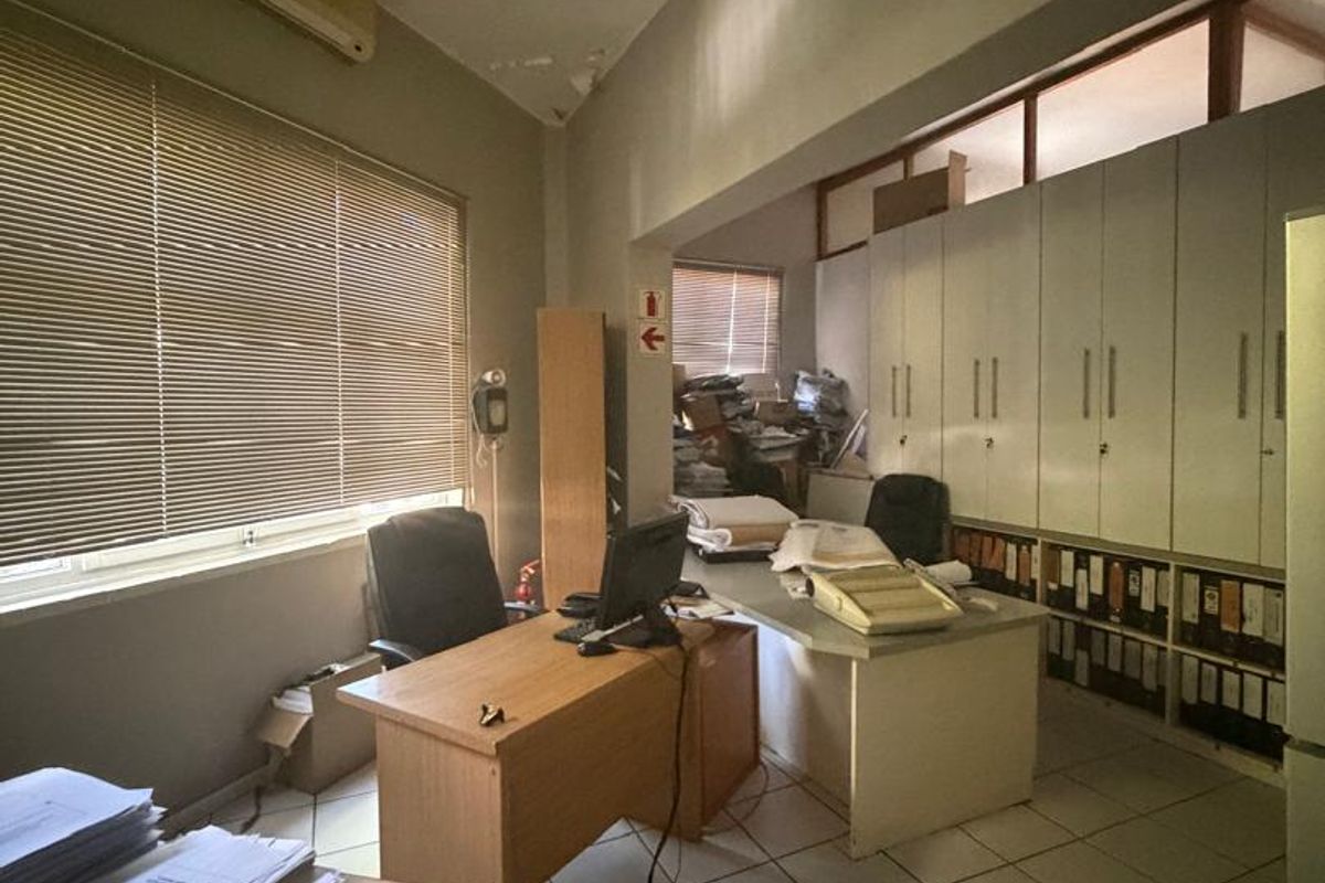 A functional office space featuring built-in storage cabinetry, tiled flooring, and a wall-mounted air conditioning unit, currently used as a workspace.