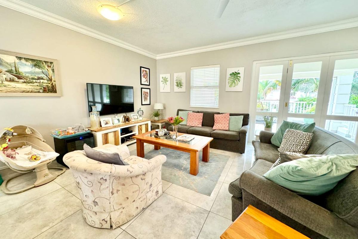 A bright living room featuring tiled flooring, crown molding, and double french doors providing access to the outdoor area.