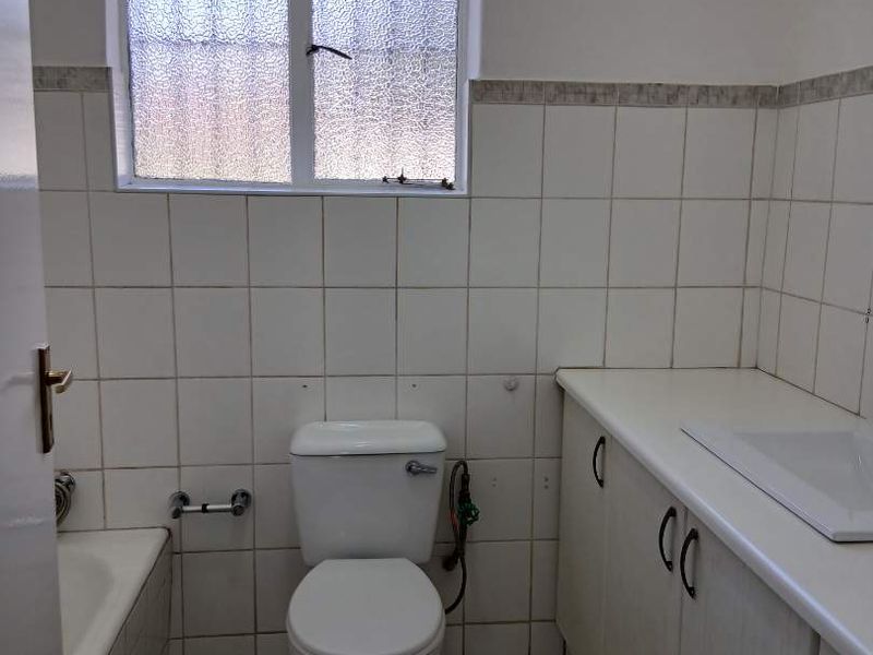 A functional bathroom featuring a built-in vanity with basin, toilet, and bathtub, finished with white wall tiles and neutral floor tiles.