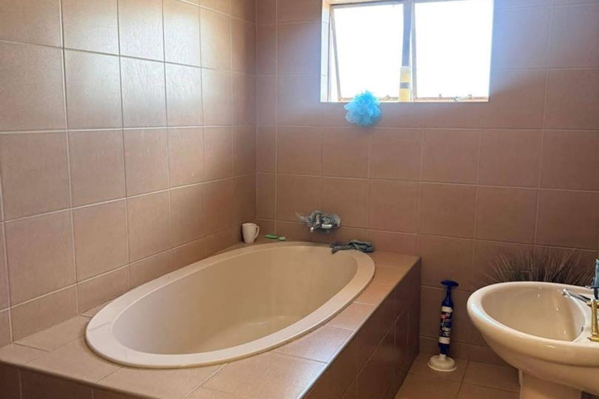 A functional bathroom featuring a built-in bathtub with tiled surround, a pedestal sink, and neutral wall tiling.