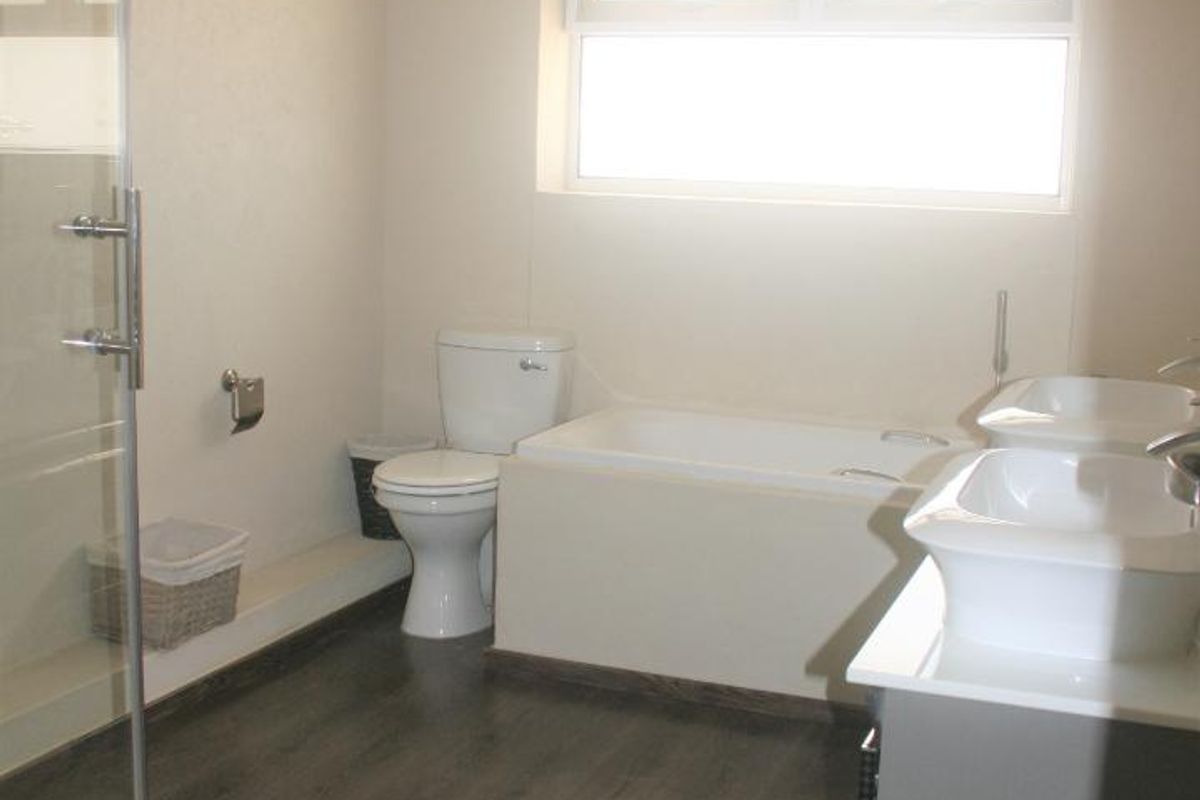 A modern bathroom featuring a glass-enclosed shower, a built-in bathtub, dual vanity basins, and dark wood-look flooring.