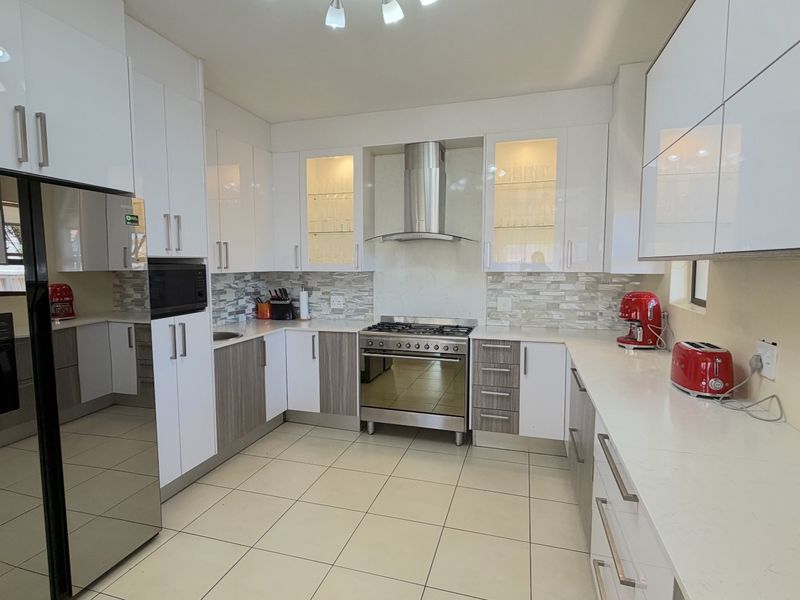 Modern kitchen featuring high-gloss white cabinetry, stone countertops, stainless steel appliances, and a stylish mosaic tile backsplash with ample storage space.