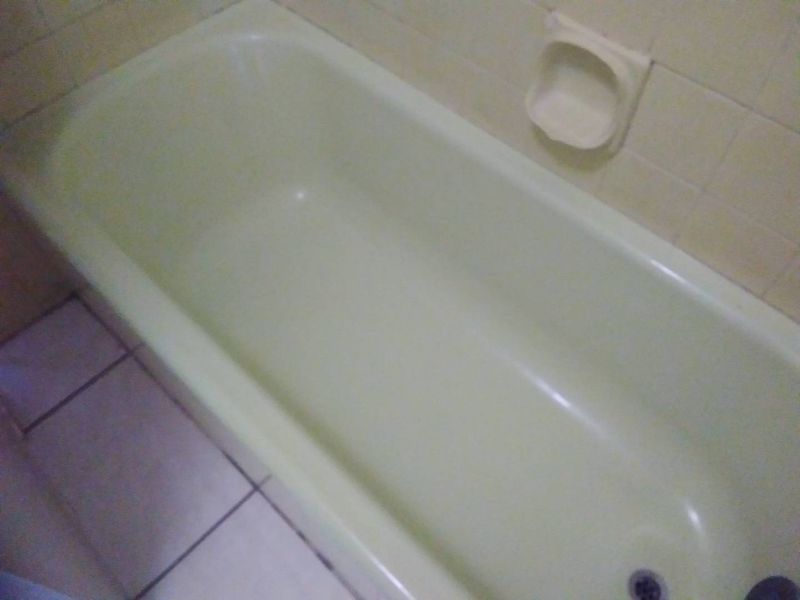 A dated bathroom featuring a standard bathtub with integrated soap dish and tiled wall and floor finishes.
