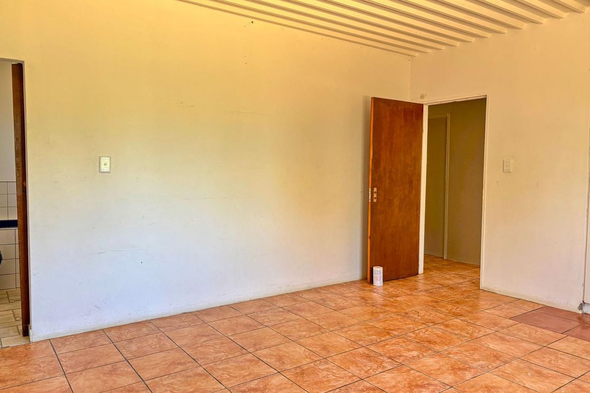 An empty living area featuring terracotta-style floor tiles, a textured ceiling, and wooden interior doors, offering a blank canvas for renovation.