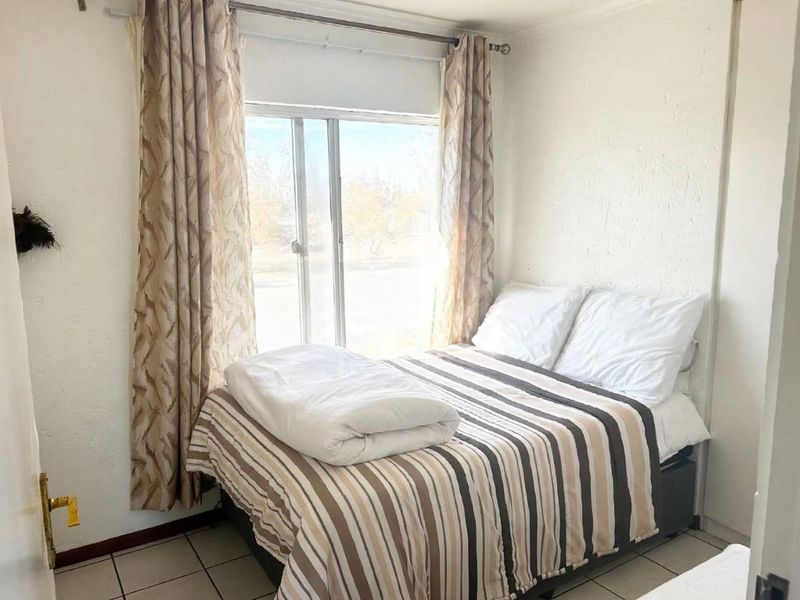 A compact bedroom featuring tiled flooring, a built-in cupboard, and a sliding window with natural light.