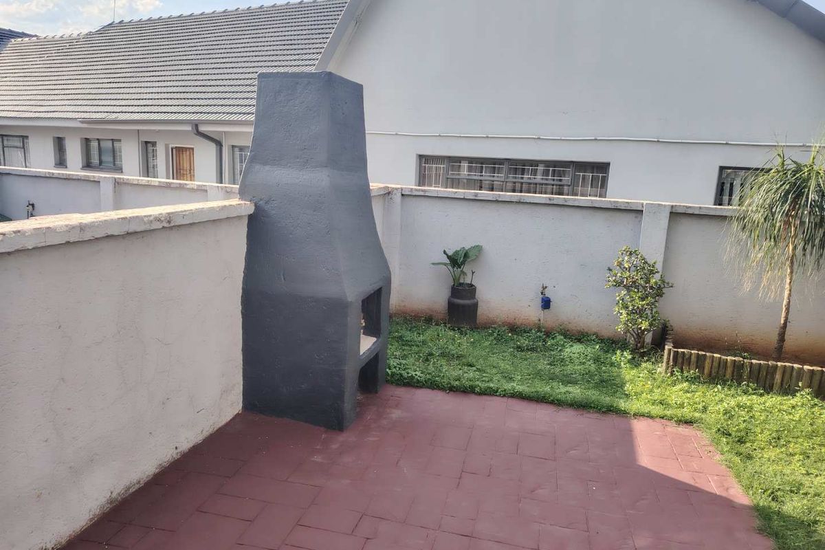 A rear courtyard area featuring a paved patio, a built-in braai, and a small lawn enclosed by a boundary wall.