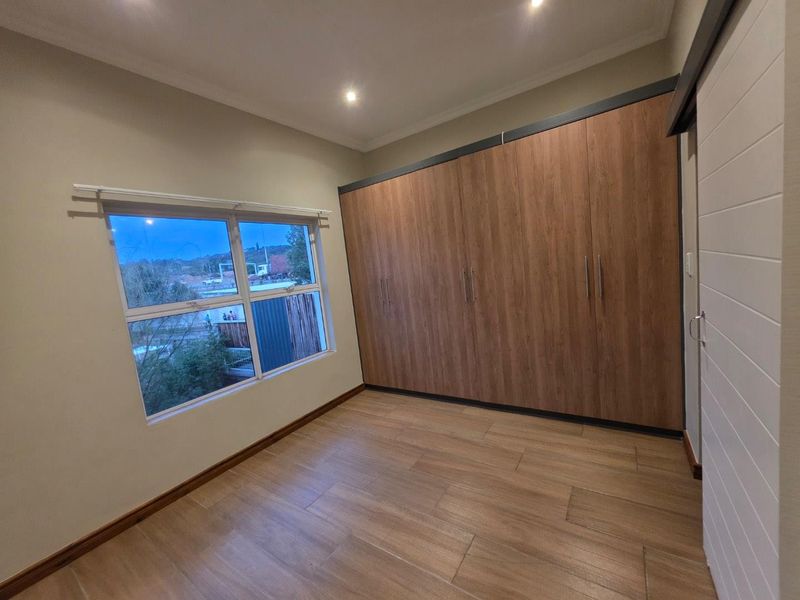 A bright, empty bedroom featuring modern wood-finish built-in cupboards, tiled flooring, and recessed downlighting.