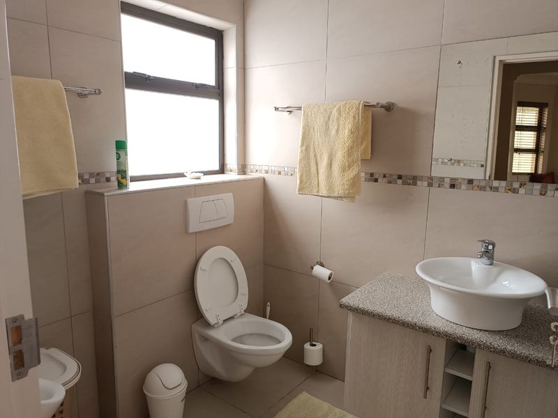 A functional bathroom featuring a wall-mounted toilet with concealed cistern, a vessel sink on a granite-topped vanity, and neutral wall tiling with mosaic accents.