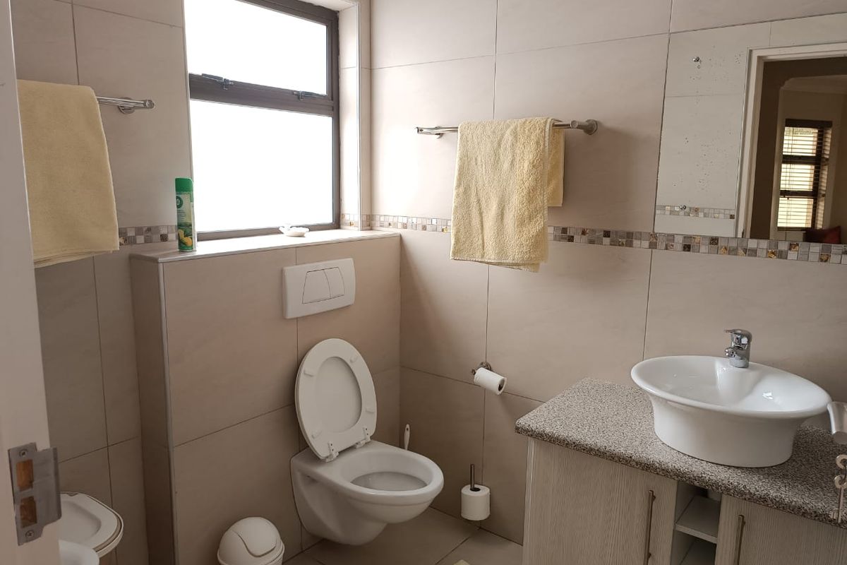 A functional bathroom featuring a wall-mounted toilet with concealed cistern, a vessel sink on a granite-topped vanity, and neutral wall tiling with mosaic accents.