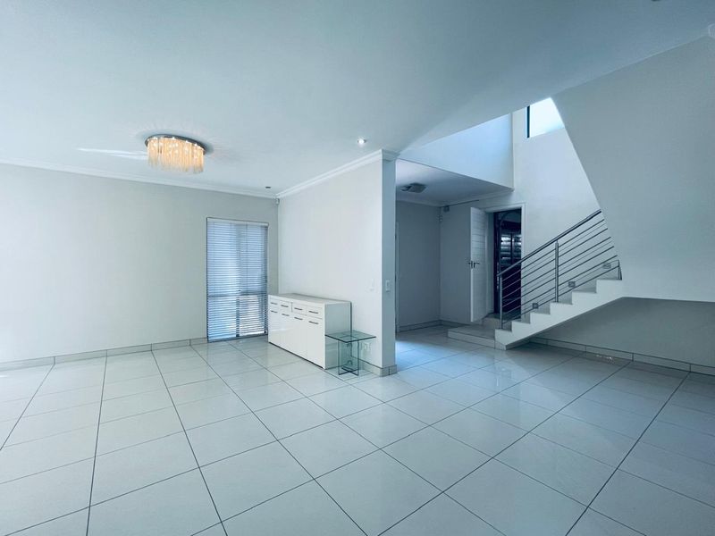 Spacious open-plan living area featuring large format floor tiles, a modern staircase with metal balustrade, and neutral finishes throughout.