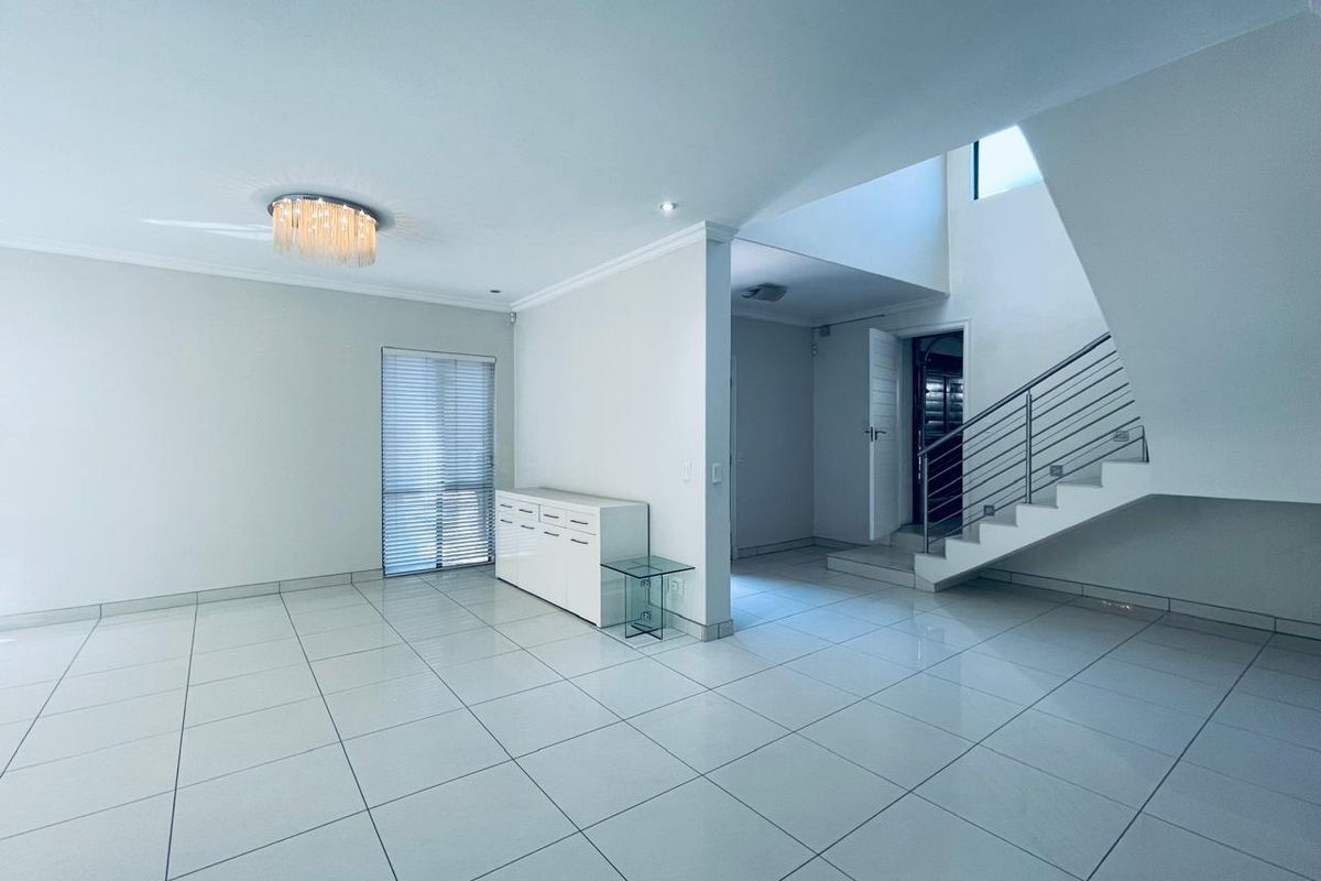 Spacious open-plan living area featuring large format floor tiles, a modern staircase with metal balustrade, and neutral finishes throughout.