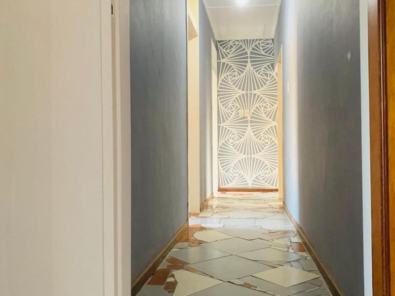 A narrow hallway featuring a decorative wall accent and damaged tiled flooring requiring repair or replacement.
