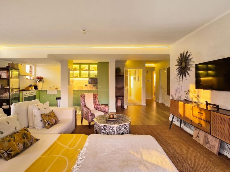 Spacious open-plan living area featuring a modern kitchen with green cabinetry, farmhouse sink, and warm ambient cove lighting throughout the connected living space.