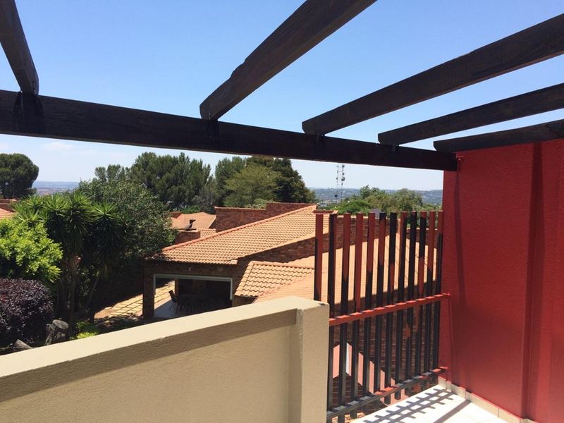 A private balcony featuring a wooden pergola structure, tiled flooring, and a metal balustrade, offering elevated views of the surrounding neighborhood.