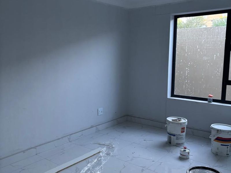 An empty bedroom currently under renovation, featuring modern tiled flooring, recessed ceiling details, and large aluminium-framed windows.