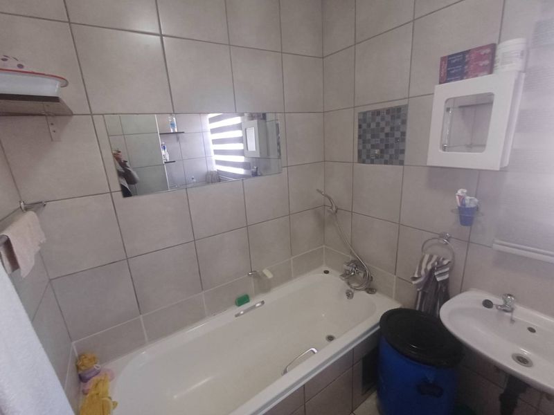 A functional bathroom featuring a bathtub with a handheld shower attachment, a wall-mounted basin, and full-height wall tiling.