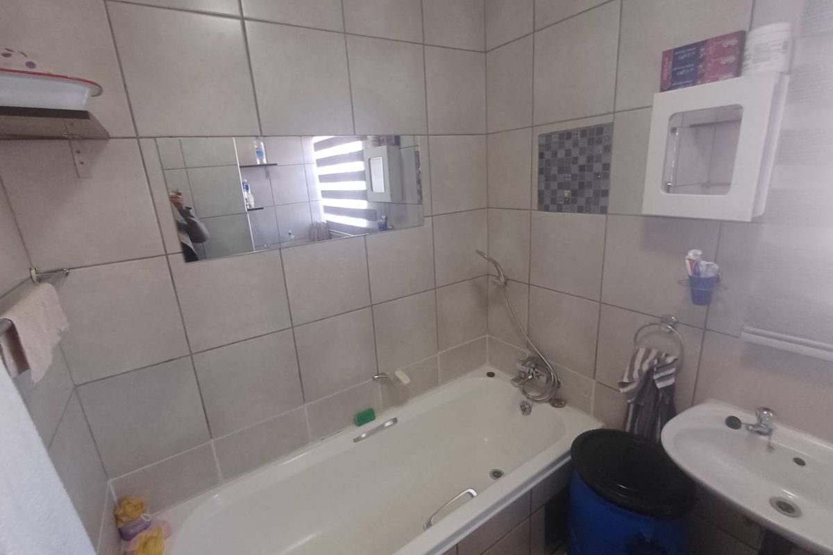 A functional bathroom featuring a bathtub with a handheld shower attachment, a wall-mounted basin, and full-height wall tiling.