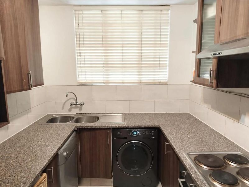 A functional kitchen featuring granite countertops, laminate cabinetry, a stainless steel double sink, and built-in electric hob with an extractor fan.