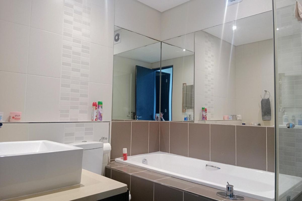 Modern bathroom featuring a built-in bathtub, vessel sink on a vanity countertop, and large wall-to-wall mirrors with neutral ceramic tiling.