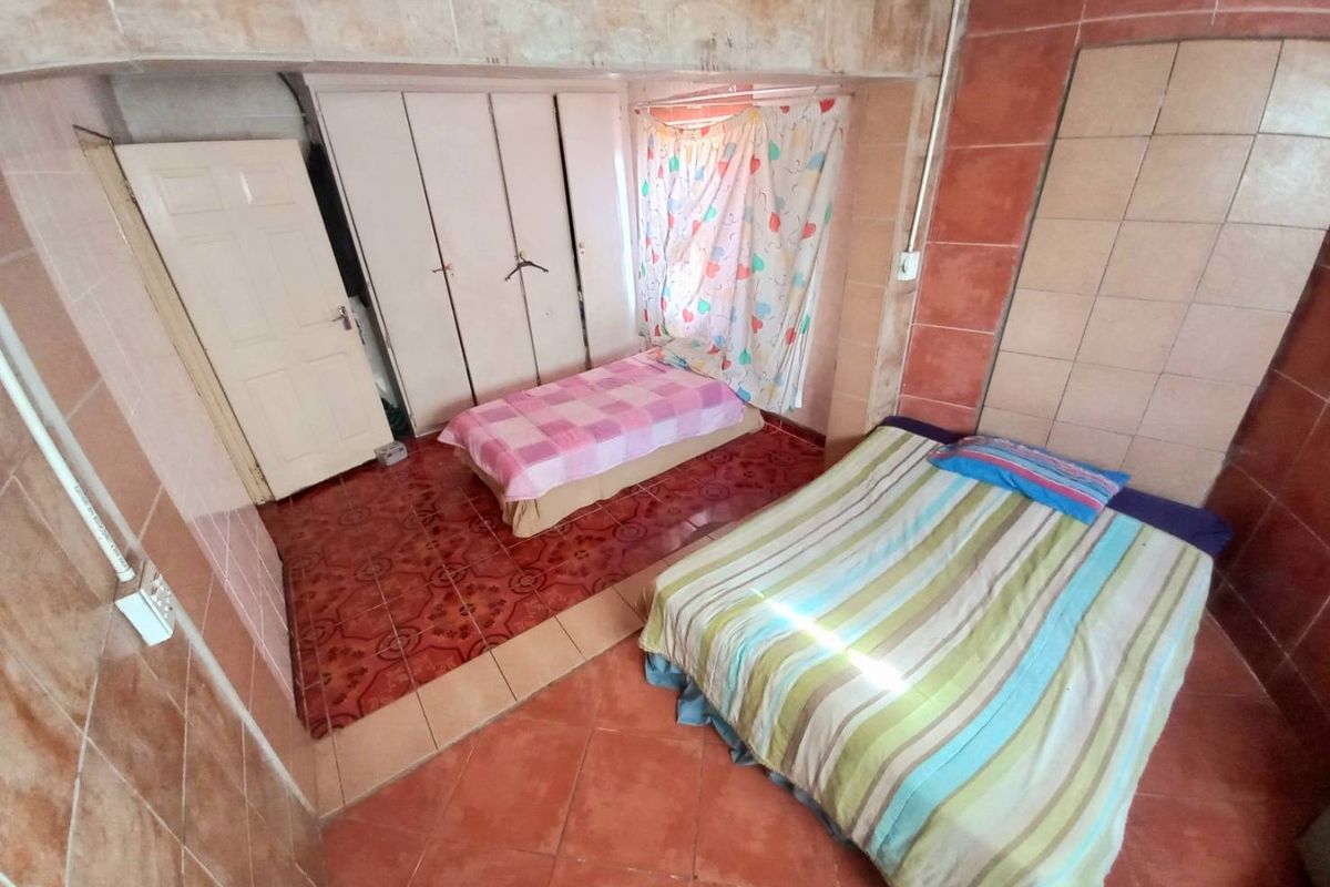 A bedroom featuring dated floor-to-ceiling wall tiles, built-in wardrobe storage, and tiled flooring.