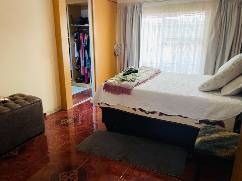 A bedroom featuring tiled flooring, a built-in wardrobe, and a window with security bars, offering a functional living space.