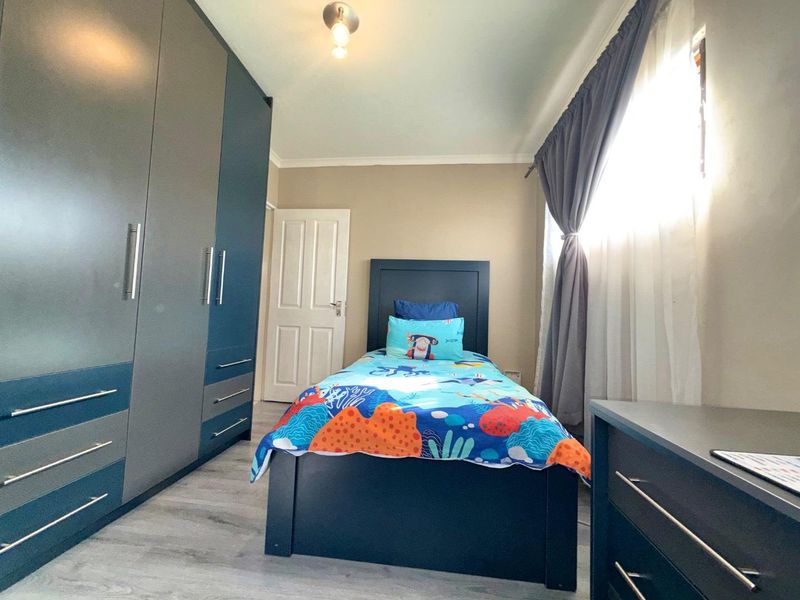 A well-maintained bedroom featuring modern built-in cupboards, laminate flooring, and neutral wall finishes, providing a functional and tidy living space.