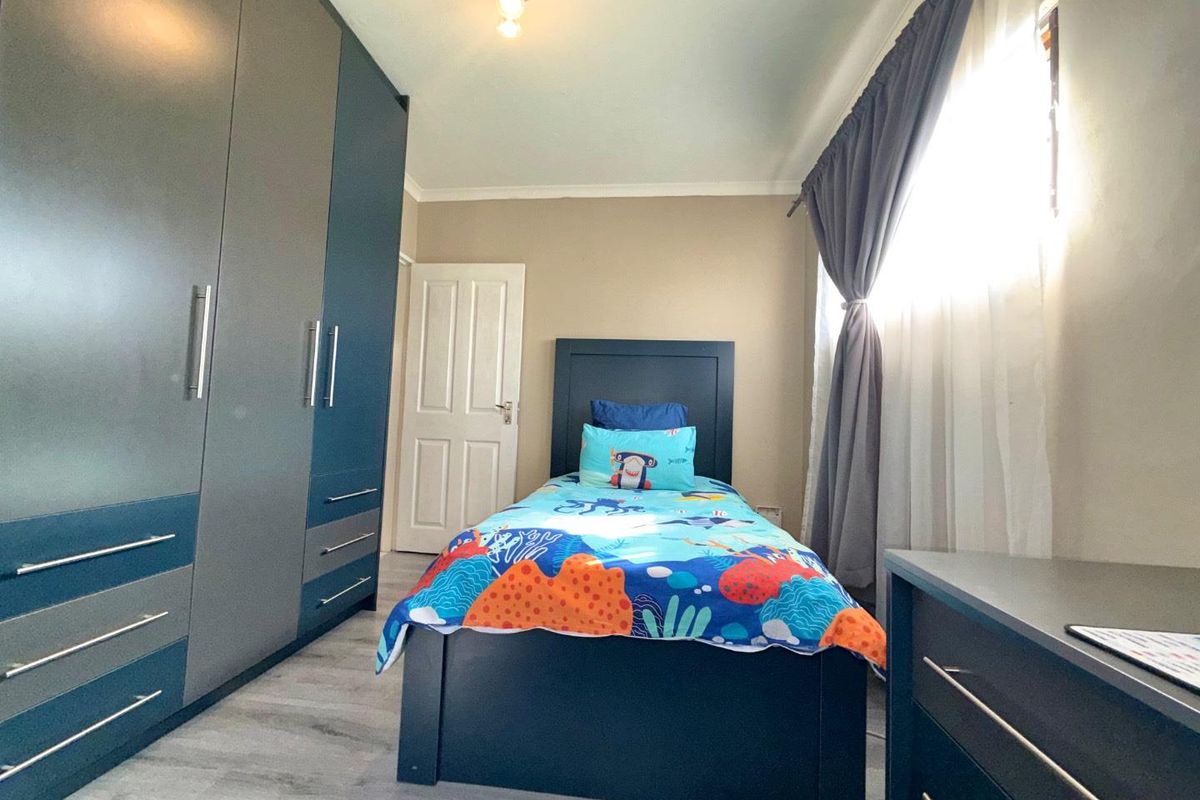 A well-maintained bedroom featuring modern built-in cupboards, laminate flooring, and neutral wall finishes, providing a functional and tidy living space.
