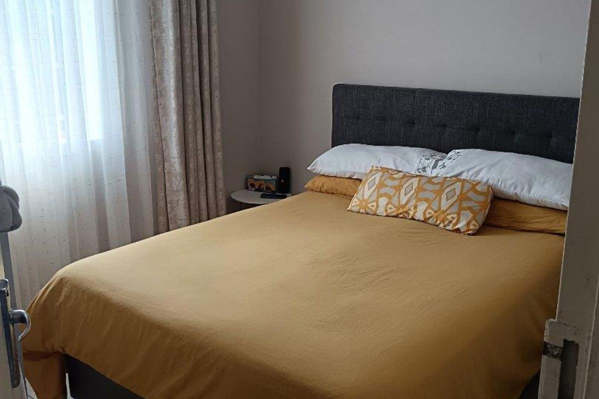 A functional bedroom featuring tiled flooring and a window with curtain fixtures.