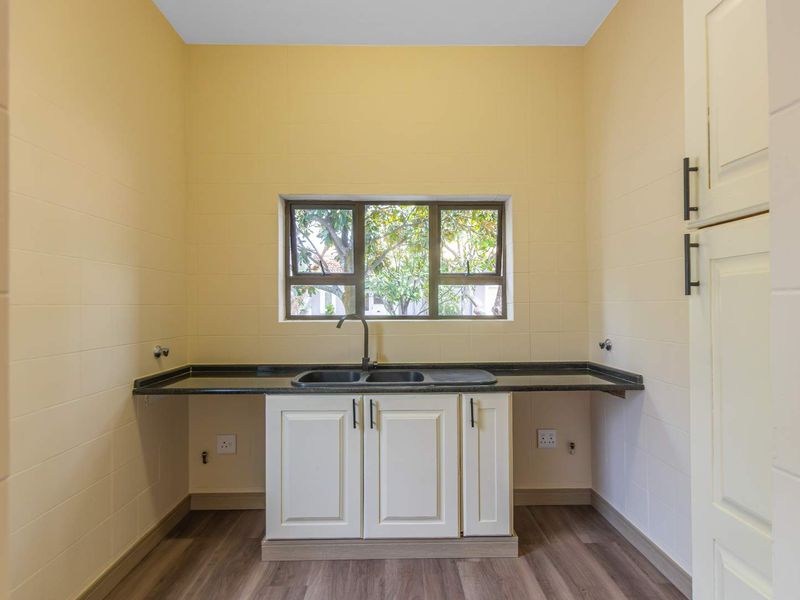 A clean and functional laundry room featuring a double basin sink, granite countertops, built-in cabinetry, and tiled walls with plumbing connections.