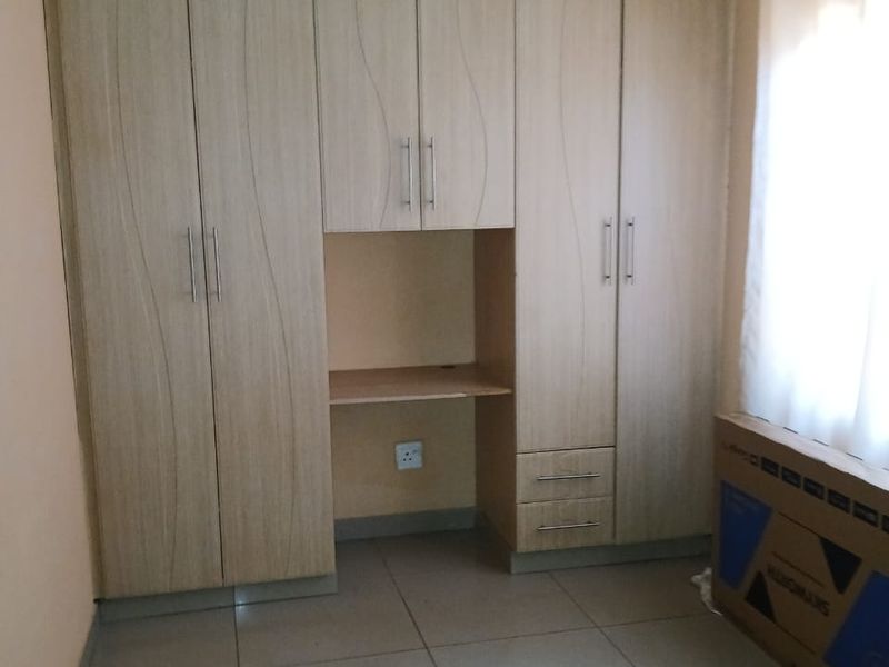 A bedroom featuring built-in wooden cupboards with an integrated desk area, tiled flooring, and a neutral color palette.