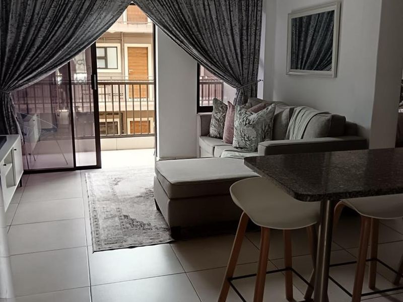 Open-plan living area featuring tiled floors, a granite breakfast bar, and a split-system air conditioner with direct access to a private balcony.