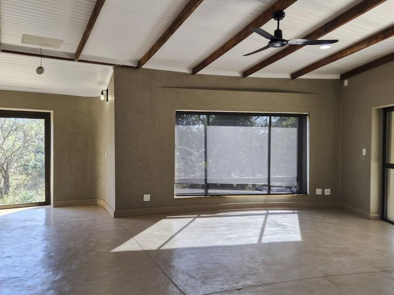 Spacious living area featuring polished concrete floors, exposed timber ceiling beams, a modern ceiling fan, and large windows providing ample natural light.