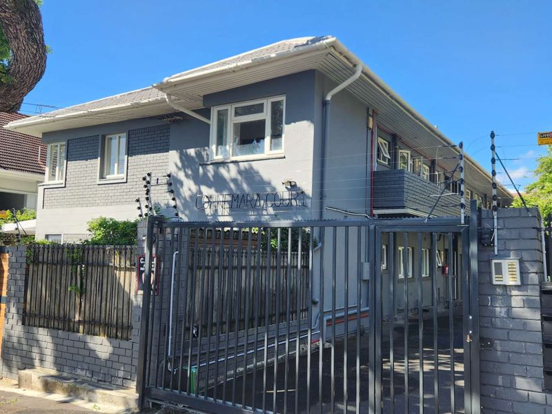 Front elevation of Connemara Court apartment building featuring grey painted brickwork, tiled roof, and secure gated entrance with electric fencing.