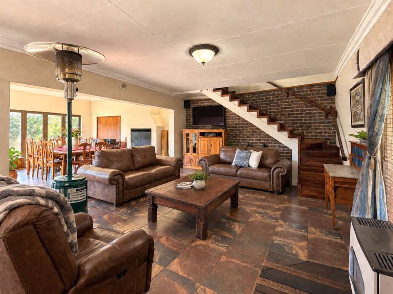 Spacious open-plan living and dining area featuring exposed brickwork, a wooden staircase, and tiled flooring, creating a warm and inviting atmosphere.