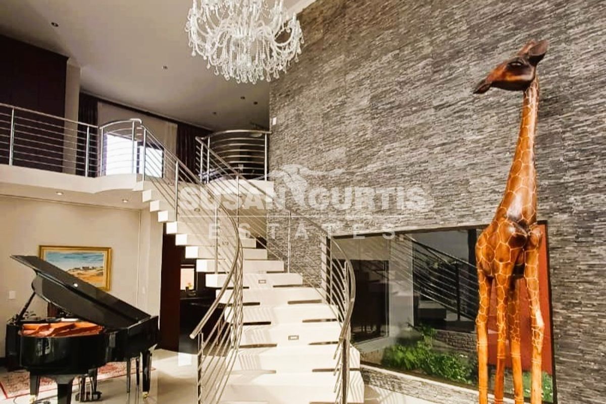 Spacious living area featuring a dramatic stone feature wall, elegant floating staircase with stainless steel balustrades, and a grand chandelier.