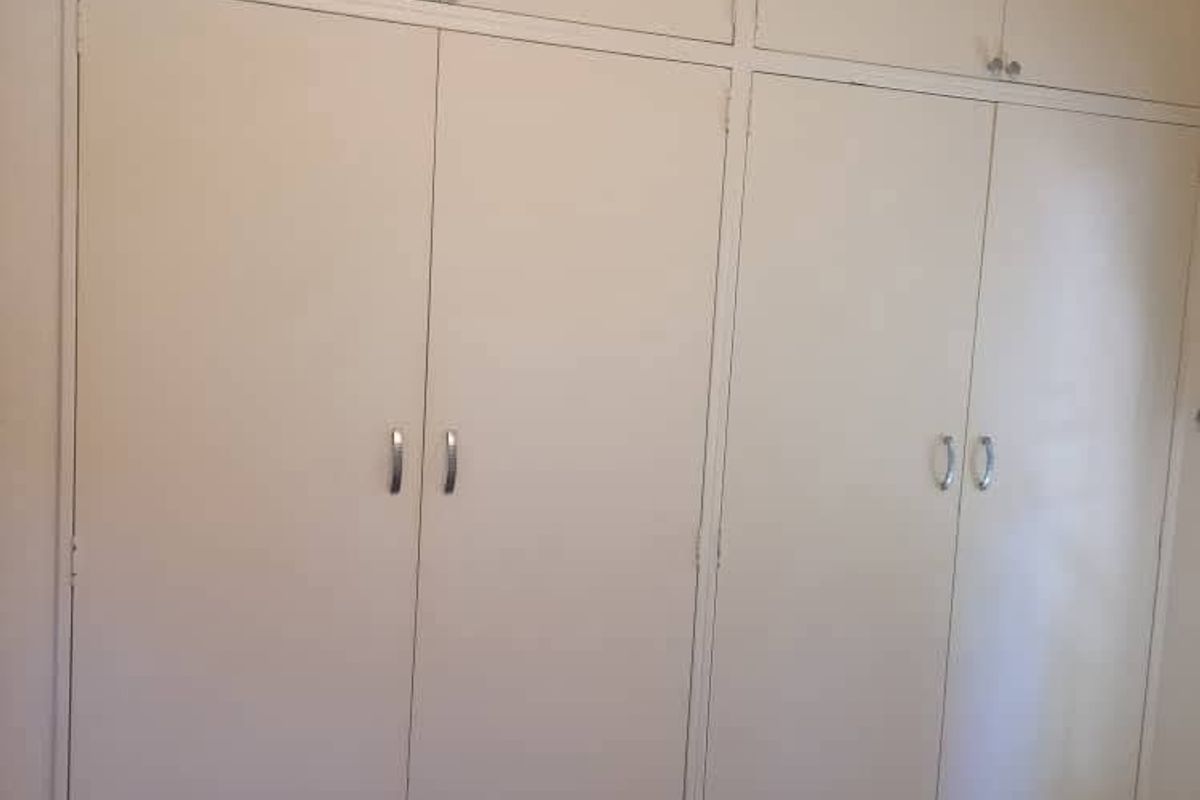 A bedroom featuring floor-to-ceiling built-in cupboards with integrated overhead storage cabinets, providing ample storage space.