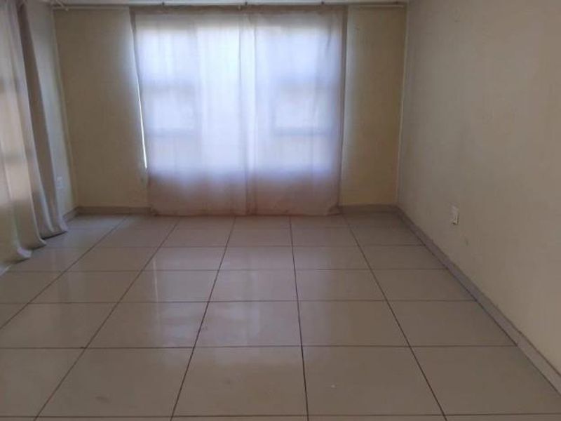 An empty living room featuring neutral tiled flooring and large windows with curtain tracks, offering a blank canvas for interior design.