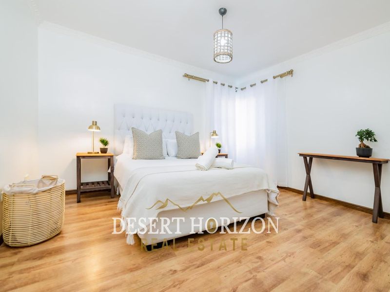 A bright and well-maintained bedroom featuring warm-toned laminate flooring, decorative cove cornicing, and a modern pendant light fixture.